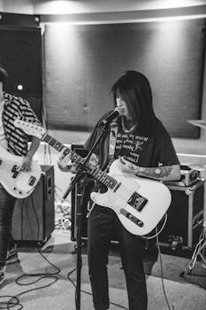 Black and white photo of a female musician passionately playing an electric guitar in a studio.