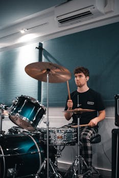 A young adult drummer plays passionately in a modern soundproof room, showcasing musical expertise.
