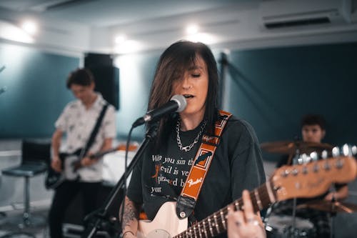 A Woman in Black Singing while Playing Electric Guitar