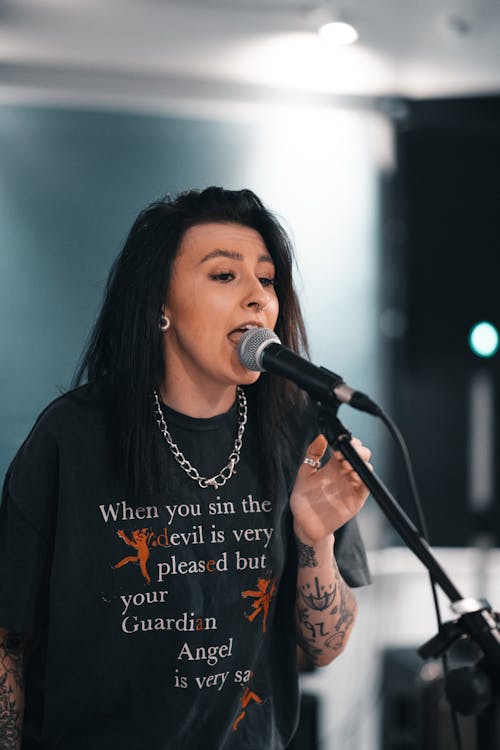 A Tattooed Woman in Black Singing with a Microphone