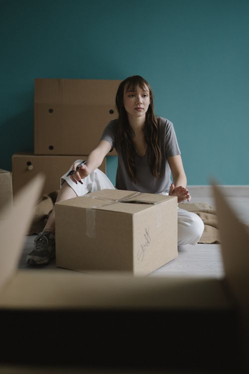 Free Woman sitting on the floor surrounded by moving boxes, suggesting a relocation or unpacking scene. Stock Photo