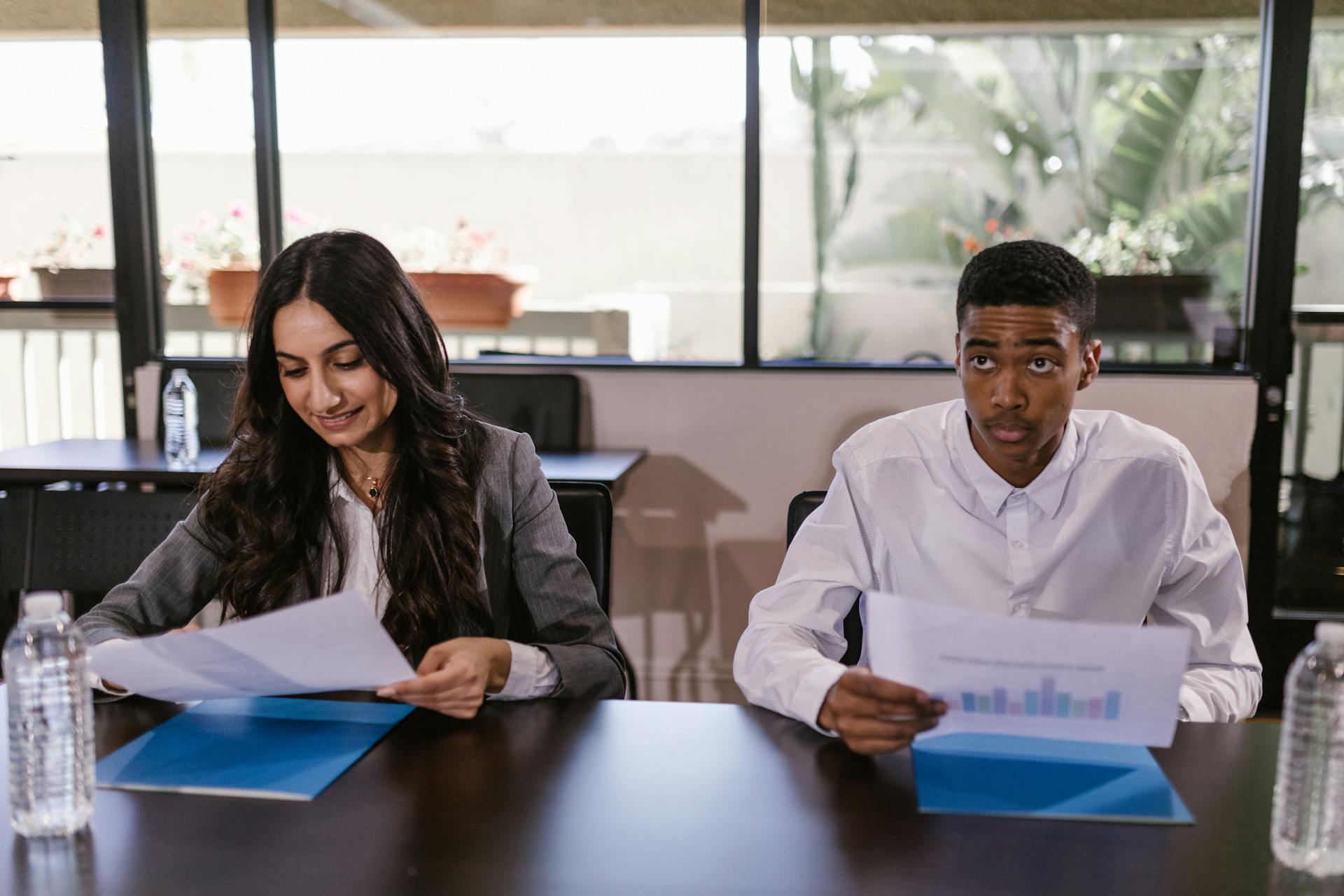 Two business professionals reviewing printed documents at a meeting table in a modern office setting.