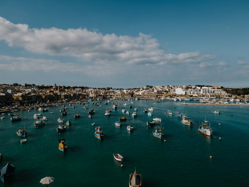 Aerial view of Marsaxlokk fishing village harbour with colourful traditional luzzu boats and coastal buildings