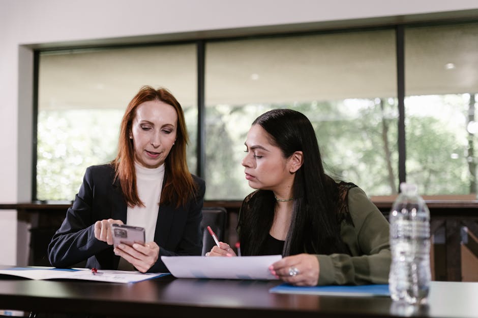 Two professional women collaborating with documents and smartphone in a meeting room.