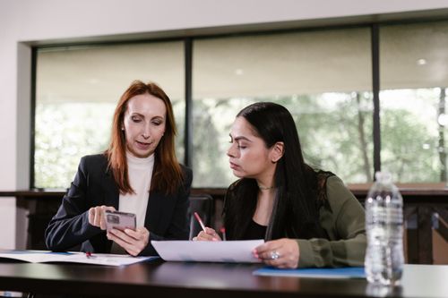 Free Two professional women collaborating with documents and smartphone in a meeting room. Stock Photo