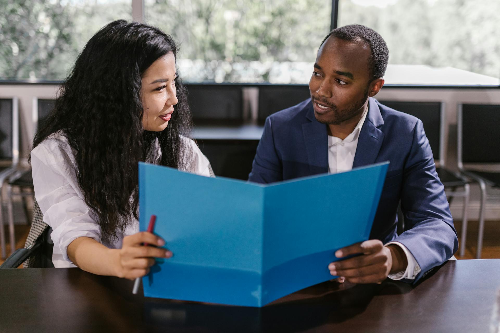 Two business professionals discussing a report in an office meeting room with natural light.