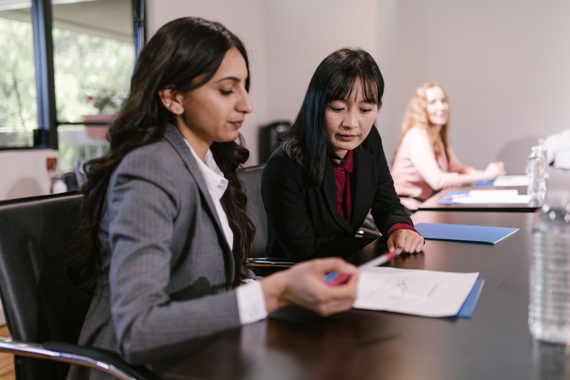 Two businesswomen discussing documents at a corporate meeting in an office setting.