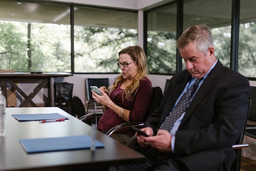 Business professionals checking phones during a meeting indoors, showcasing modern work dynamics.