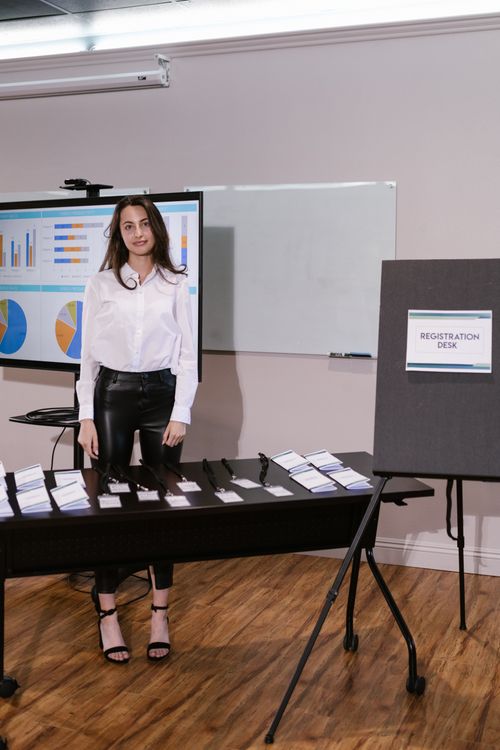 Free Woman standing at registration desk in a corporate event setting with presentation screen. Stock Photo