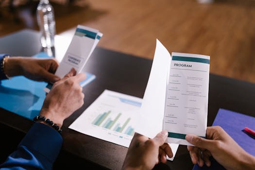 Hands examine program guide in a corporate meeting setting, highlighting agenda details.