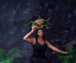 Stylish portrait of a woman in Lagos holding a woven basket with tropical plants and fruits.