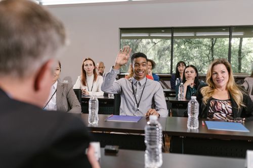 Free Businesspeople in a conference room engaging in a discussion, with a man raising his hand. Stock Photo