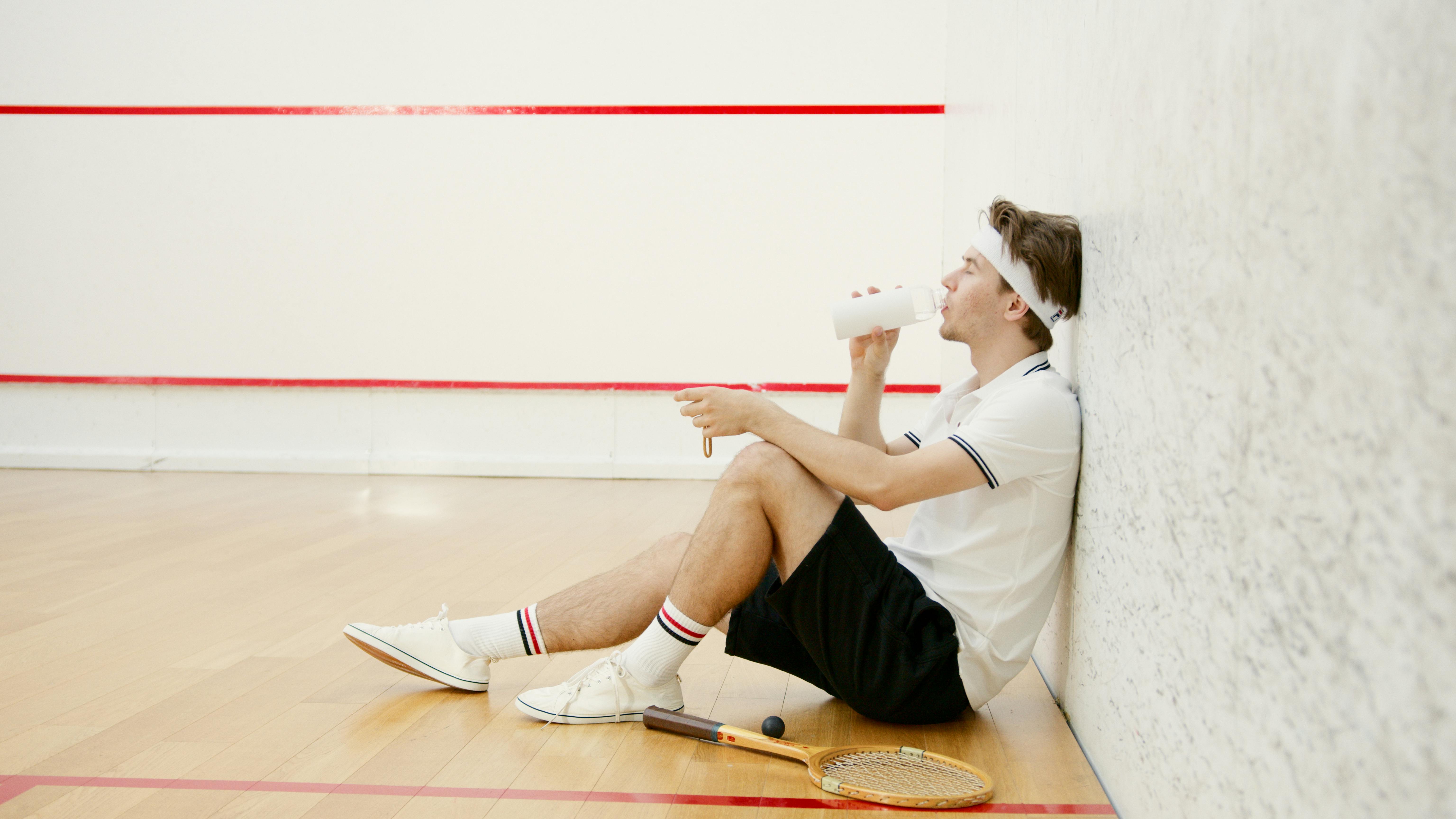 side view of a squash player drinking water while resting