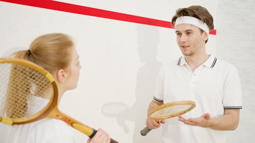 A young man and woman enjoying a squash game indoors, focusing on fitness and fun.