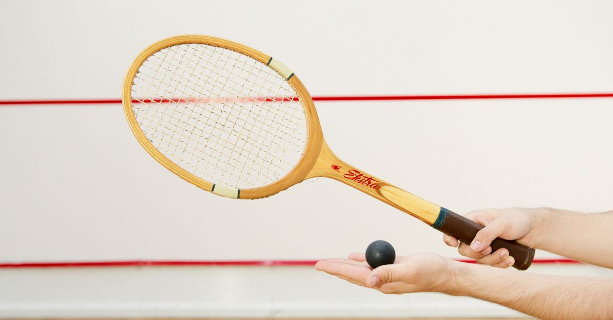 Detailed view of a squash racket and ball in hand, indoor sports scene.