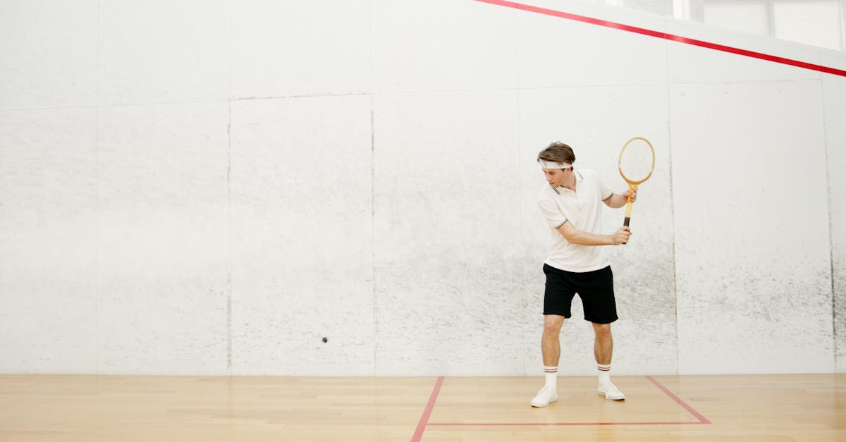 A male squash player in action, ready to strike a ball in an indoor squash court.