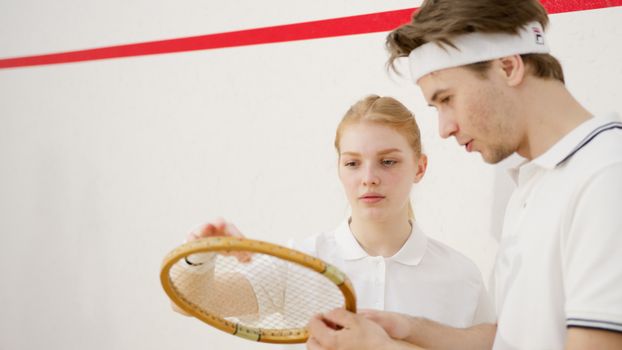 Young squash players discussing techniques on the court with focus on a racket.