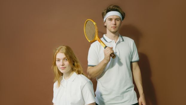 Portrait of a young male and female tennis players in white attire posing indoors with a vintage racket.