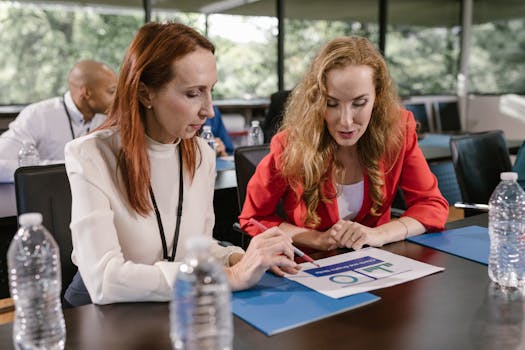 Two women engaged in a business meeting, discussing documents in a well-lit office.