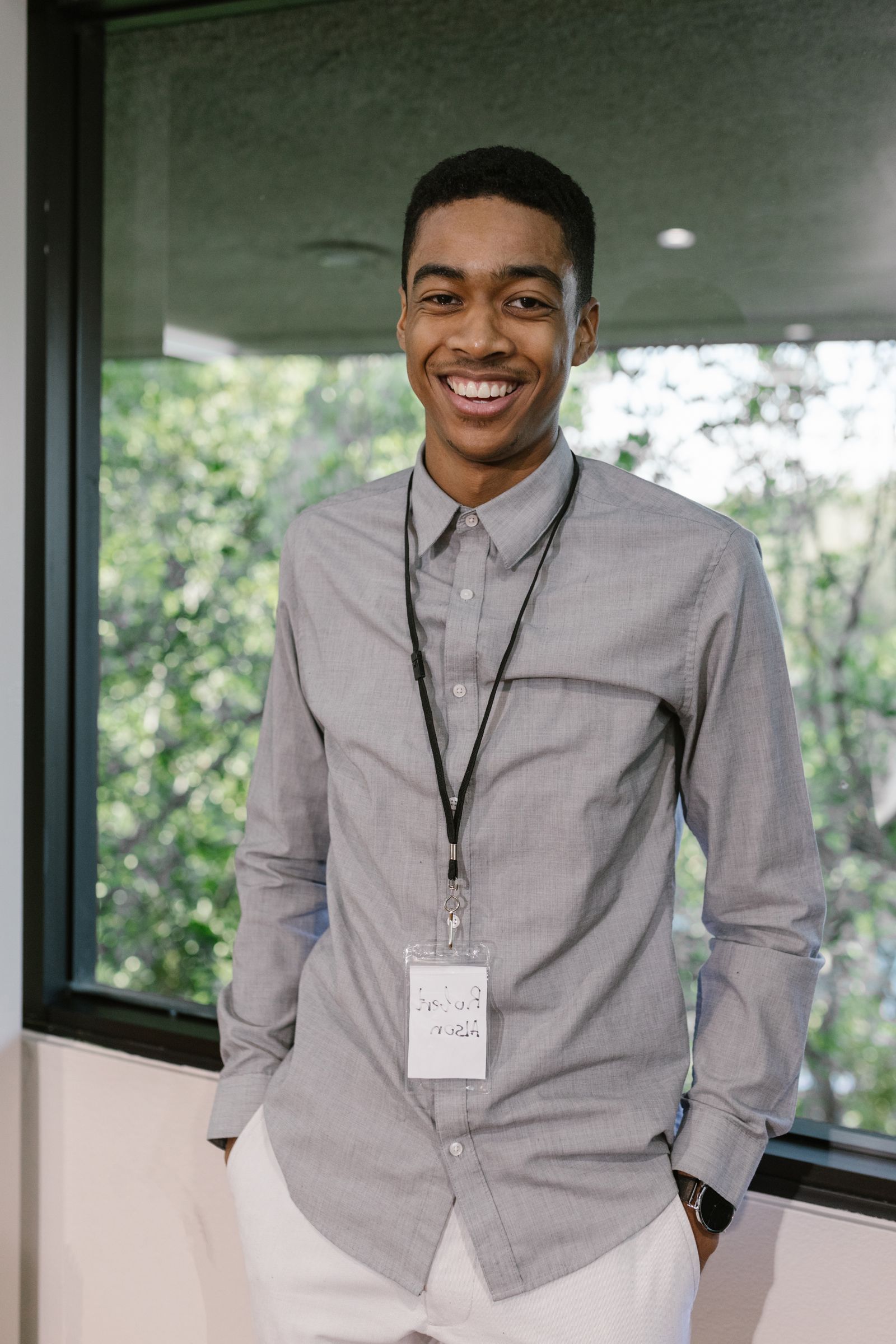 A young man in a grey shirt standing by an office window
