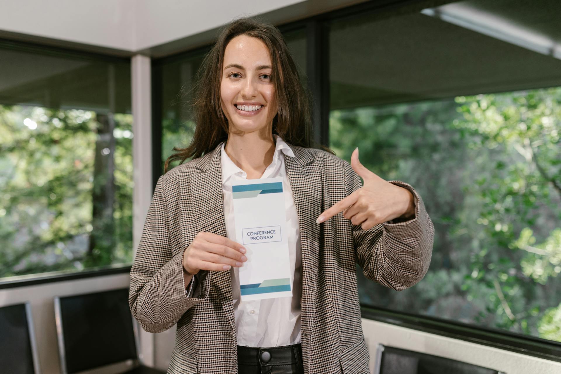 Woman indoors holding and pointing at a conference program pamphlet with a smile.