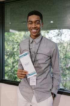 Smiling young man holding a conference program at an indoor corporate event.