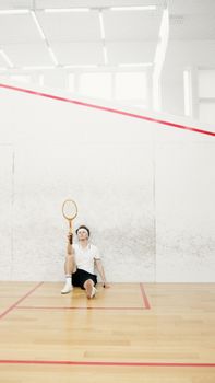 A squash player in sportswear sitting and resting on an indoor court.