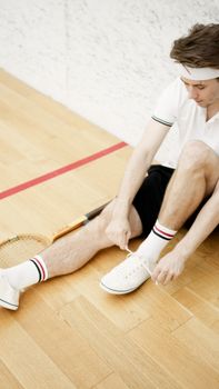 Young tennis player preparing on indoor court, tying shoelaces.