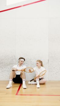 A young couple relaxing with squash rackets on an indoor court, capturing leisure and fitness.