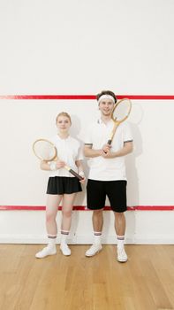 Two squash players posing with rackets in a bright indoor court, showcasing teamwork and sports gear.