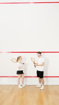 A young man and woman practice squash on an indoor court, holding rackets and wearing sports attire.
