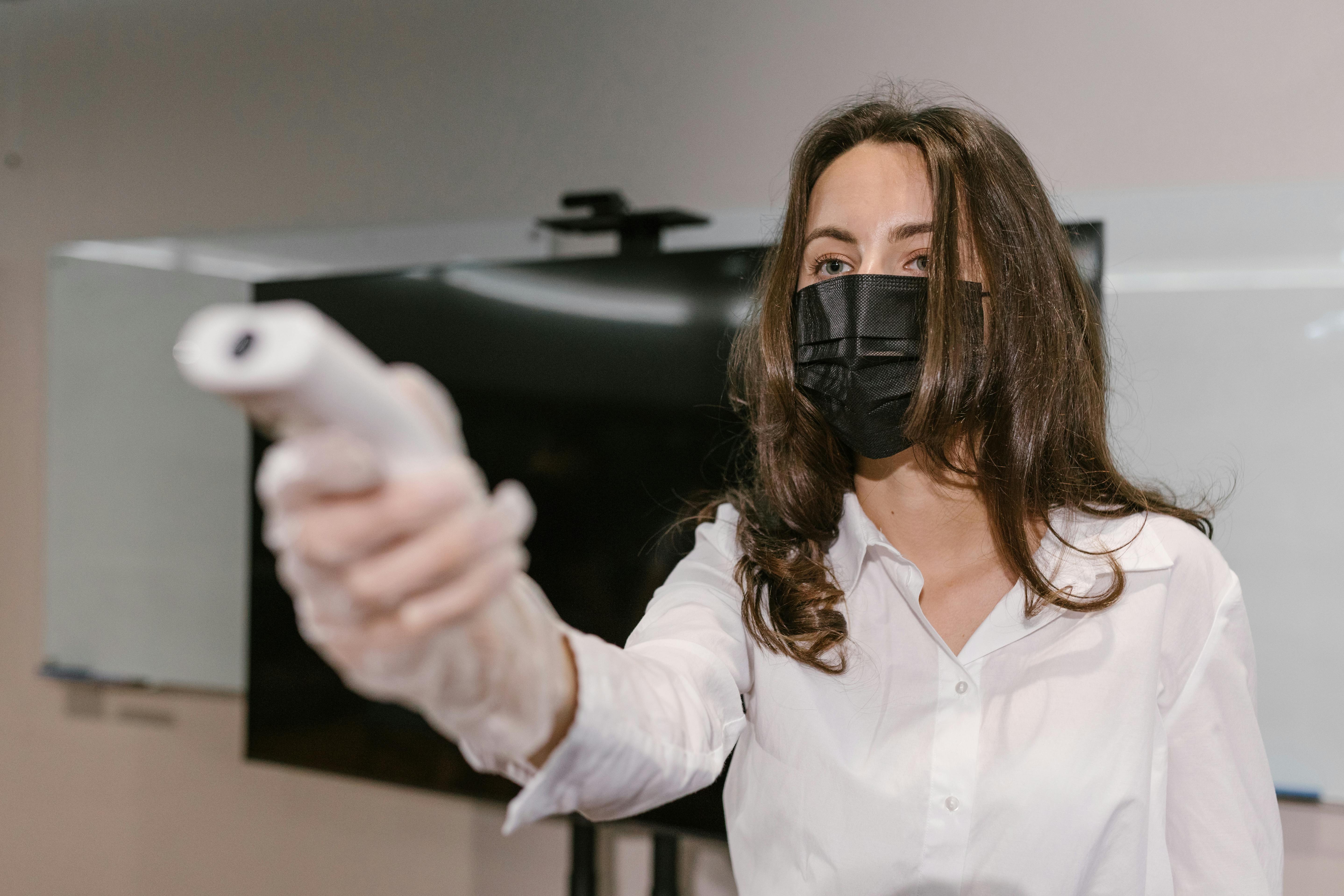 Woman wearing face mask using an infrared thermometer indoors.