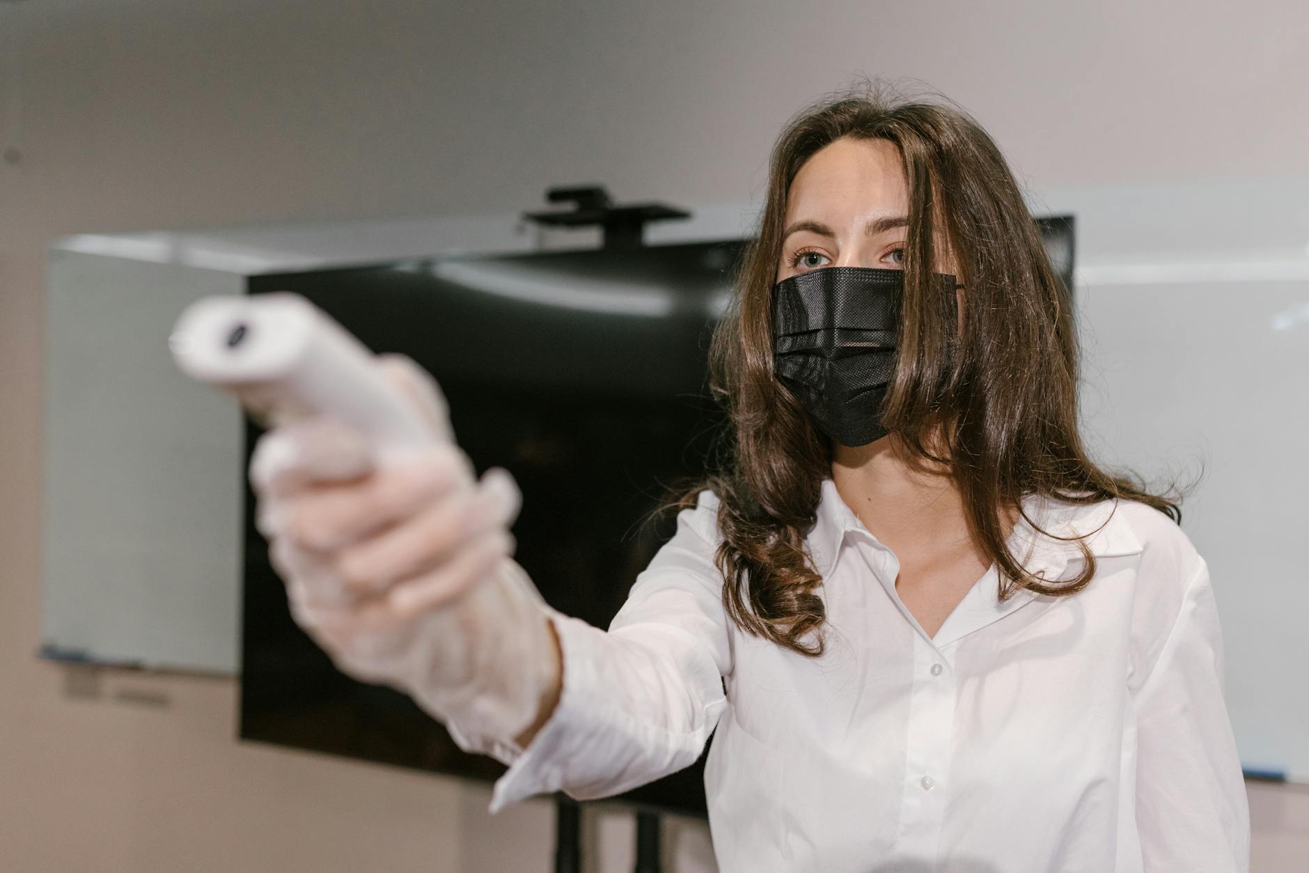 Woman wearing face mask using an infrared thermometer indoors.