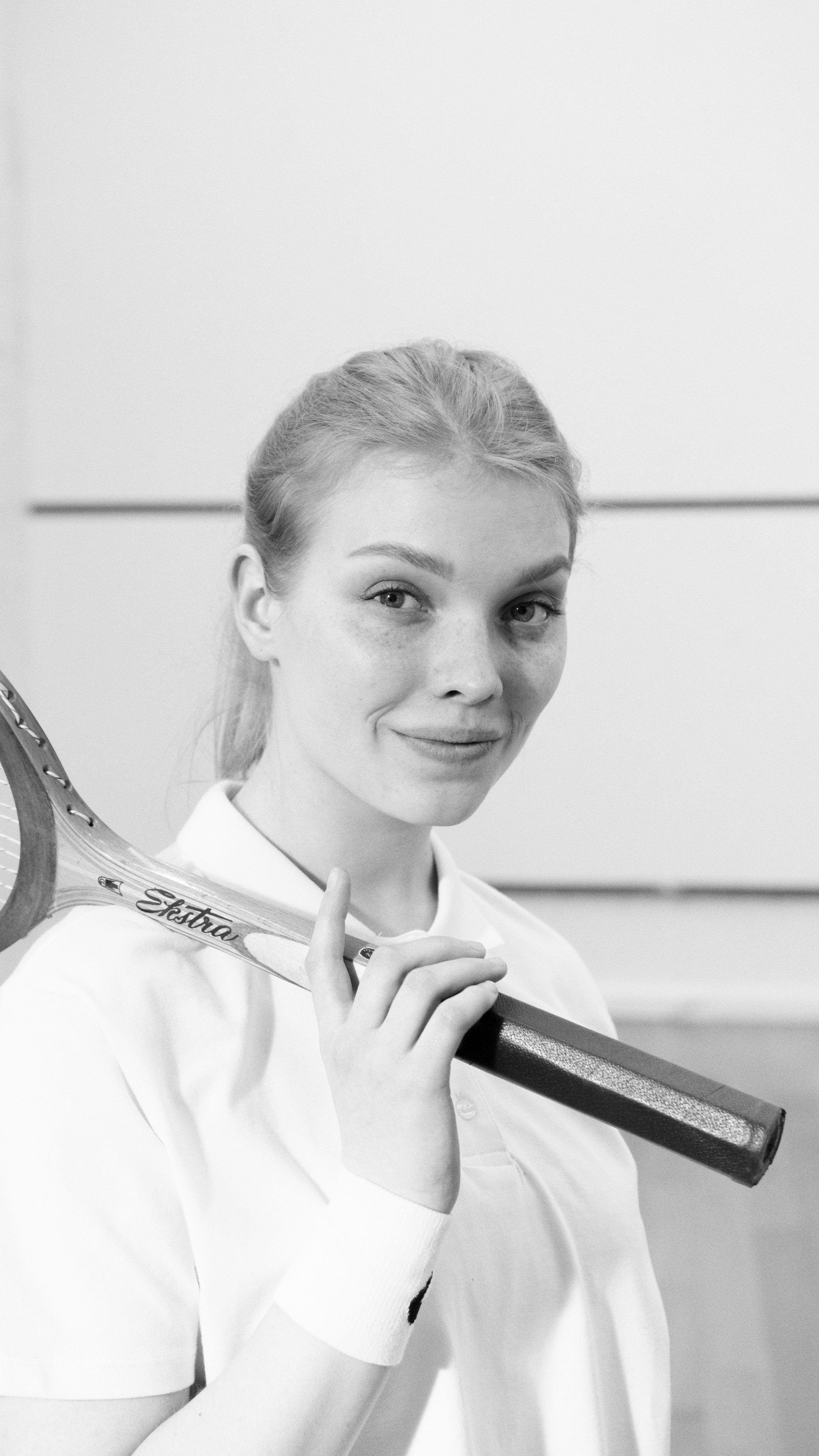 Elegant black and white portrait of a woman holding a tennis racket indoors.