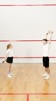 A man and woman in sportswear exercise with squash rackets on an indoor court.