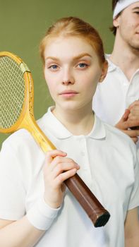Portrait of a young woman in sportswear holding a vintage tennis racket, looking confident and focused.