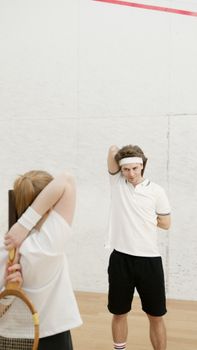 Two tennis players warming up by stretching on an indoor court, focusing on pre-game preparation.