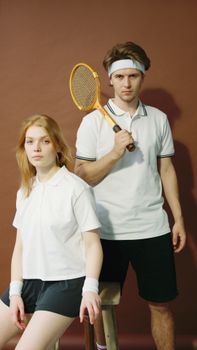 A stylish duo posing in vintage tennis attire with rackets and accessories.