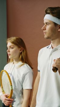Portrait of young tennis players wearing white outfits and holding rackets, set against a neutral background.