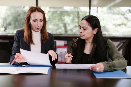 Free Two professional women reviewing documents in a well-lit office setting. Stock Photo
