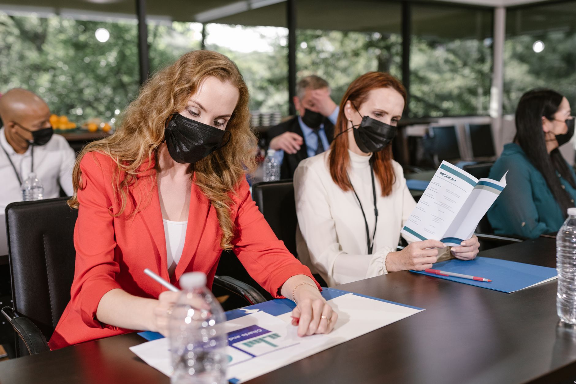 Participants in a business conference wearing face masks, taking notes indoors.