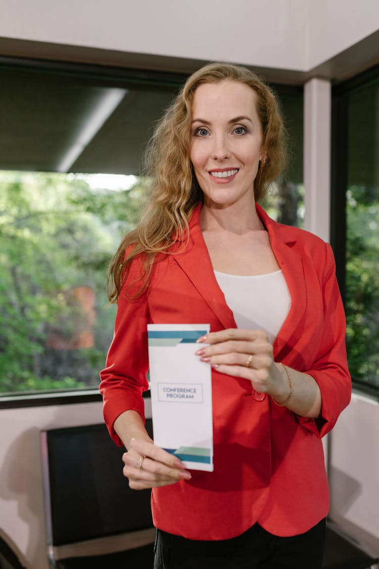 A Woman In A Red Blazer Holding A Conference Program Pamphlet