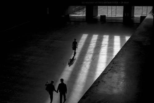 Фотография троих мужчин, идущих внутри здания в оттенках серого