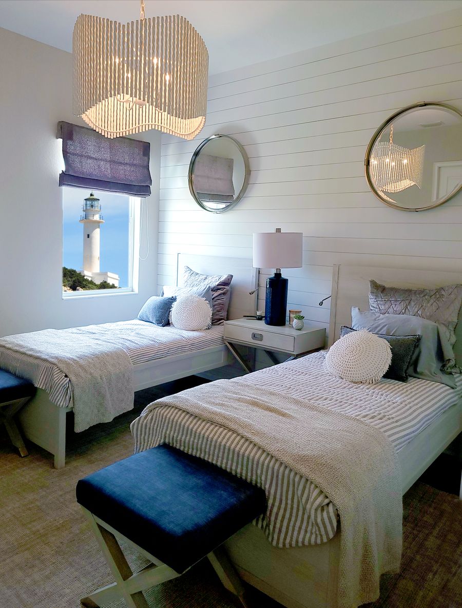 A bright twin room with shiplap walls and a window looking out to a white lighthouse