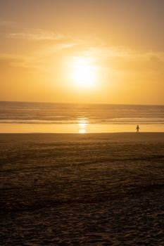 Silhouetted person walking on Costa da Caparica beach during a breathtaking sunset.