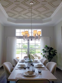 Stylish dining room featuring elegant decor, modern chandelier, and large window view.
