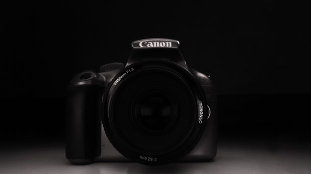 Minimalist black and white portrait of a DSLR camera with lens cap on a dark background.