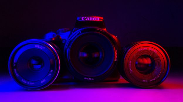 Close-up shot of camera and lenses under dramatic red and blue lighting.