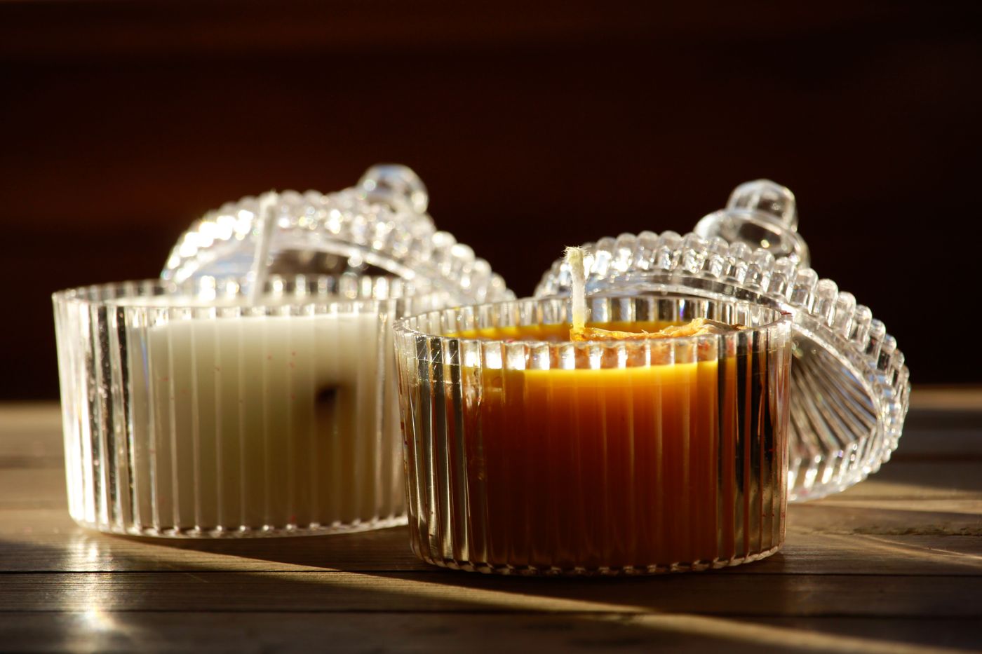 Two unlit candles in ribbed glass containers with their lids behind them.
