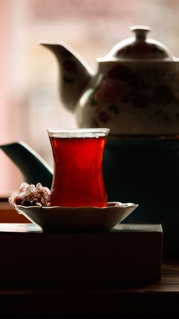 Two tulip-shaped glasses of dark reddish-brown Turkish tea on saucers with sugar cubes, next to a double-stacked çaydanlık teapot.